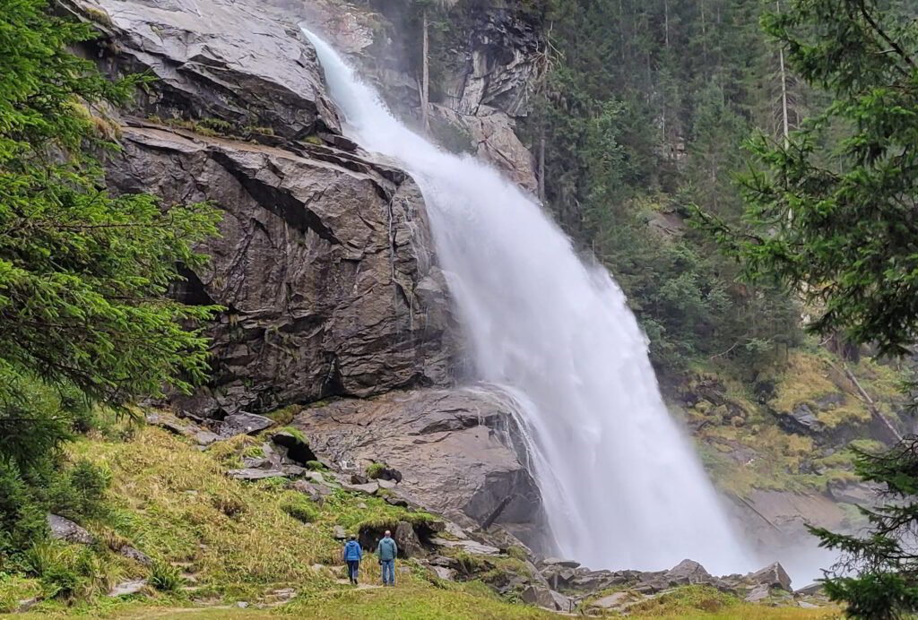 Kaksi ihmistä seisoo Krimmler vesiputousten edessä