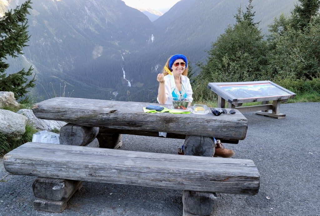 a woman enjoy mountain view and eat fruits by Gerlos Alpine road. Behind can be seen Krimmler waterfalls